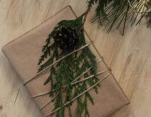 Szary papier przykryty zieloną gałązką i szyszką - to idealne opakowanie dla lubiących styl eko. 